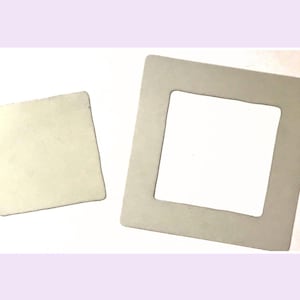 May include: A light beige square piece of material and a larger light beige square frame with a square cutout in the centre. Both items have smooth, flat surfaces and rounded corners, appearing as separate components of a set.