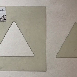 May include: Two white plastic triangle stencils. The larger stencil is approximately 25 cm tall and the smaller stencil is approximately 12.5 cm tall.