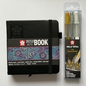 Sakura quadratisches Skizzenbuch mit schwarzen Seiten und x3 08 gemischten Gelly Roll-Stiften. Gold, Silber & weiß