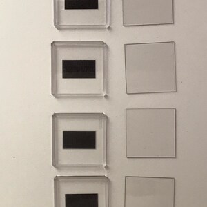 May include: Four clear plastic frames with black rectangular inserts. Each frame is paired with a blank clear plastic square.