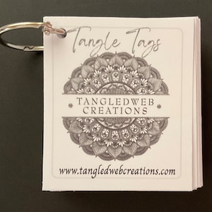 May include: A stack of white cards with a silver ring binder. The cards have a black and white mandala design with the text "Tangle Tags" and "Tangledweb Creations" and the website "www.tangledwebcreations.com".