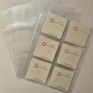 May include: Six clear plastic sleeves with white cards inside. Each card has a red square with the word "zentangle" in black text. The cards also have the text "zentangle.com" printed on them.