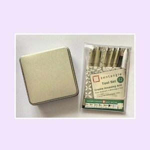 May include: A square, metallic gold-colored storage tin next to a clear plastic sleeve containing a Zentangle Tool Set 12. The set includes several pens with tan caps, a black pen, a white pencil, and a card labeled Zentangle Tool Set 12.