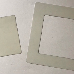May include: Two white square frames with a cutout in the centre. The smaller frame is inside the larger frame.