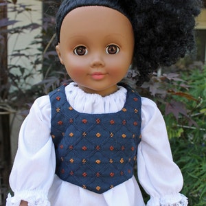 May include: A doll with dark brown skin and curly black hair is wearing a white blouse with lace trim and a blue vest with a geometric pattern.