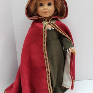 Może przedstawiać: Czerwony płaszcz z kapturem, złotą lamówką i białą podszewką. Płaszcz nosi lalka z czerwonymi włosami i zieloną sukienką.