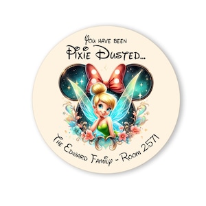 May include: A round door hanger featuring an illustration of Tinkerbell. The text "You have been Pixie Dusted..." is at the top of the hanger. The text "The Edward Family - Room 2571" is at the bottom of the hanger.