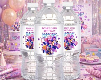 May include: Three clear plastic water bottles with white caps. Each bottle has a label that reads "Rosie's 10th Birthday KPOP" with a graphic of a group of people. The bottles are on a pink surface.
