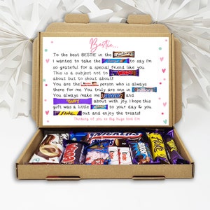 Puede incluir: Una caja de regalo de cart&oacute;n llena de varias barras de chocolate y caramelos. La caja tiene un mensaje impreso con nombres de barras de chocolate. La tapa abierta revela los dulces en el interior.