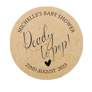 May include: Round brown paper sticker with the text "Michelle's Baby Shower" and "Ready to pop!" with a small black heart and the date "22nd August 2023".