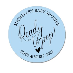 May include: Light blue circle sticker with the text "Michelle's Baby Shower" and "Ready to pop!" in black script. The date "22nd August 2023" is printed below the text with a small black heart.