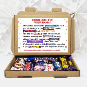 May include: A brown cardboard box with a message that says "Good Luck for Your Exams!" and is decorated with colourful candy bar wrappers. The box is open and filled with various chocolate bars, including Galaxy, Wispa, Twirl, Snickers, Boost, and Flake.