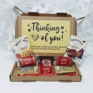 May include: A brown cardboard box with a yellow card that says "Thinking of you!" and a heart. The box is filled with various chocolate and biscuit snacks, including Lotus Biscoff, Lindor, and Yorkshire Gold.