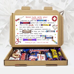 Puede incluir: Una caja de cart&oacute;n marr&oacute;n con la tapa abierta, que revela una variedad de barras de chocolate. La caja tiene un mensaje escrito a mano en el interior que dice "&iexcl;Mucha suerte con tu operaci&oacute;n!" e incluye una lista de nombres de barras de chocolate como "Wispa", "Galaxy", "Twirl", "Boost" y "Snickers".