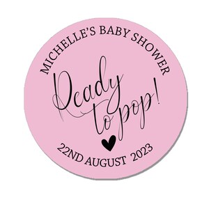 May include: Pink round sticker with black text that says "Michelle's Baby Shower Ready to Pop! 22nd August 2023".