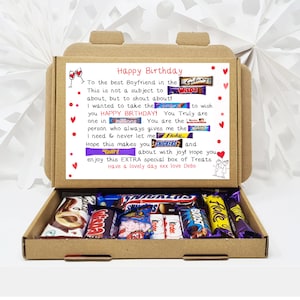 May include: A brown cardboard box with a handwritten message inside. The message says "Happy Birthday" and includes a list of chocolate bar names. The box is open and filled with various chocolate bars.