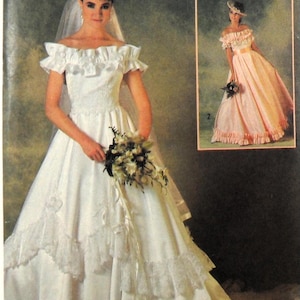 Puede incluir: Un vestido de novia blanco con un escote de volantes y una larga cola. El vestido tiene un corpiño ajustado y una falda completa. La novia lleva un ramo de flores blancas.