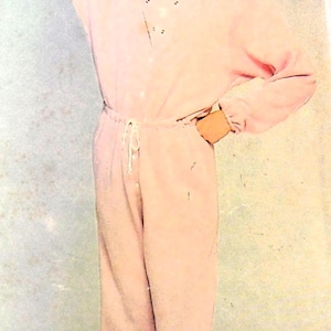 May include: A woman wearing a pink jumpsuit with a drawstring waist. She is smiling and has her hand on her hip.