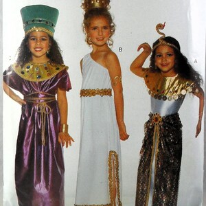 May include: Three costumes featuring historical themes. One is a purple dress with a gold collar and tall green hat. Another is a white one-shoulder dress with gold trim. The third is a gold and black outfit with a snake headpiece and coin collar.