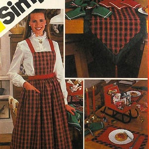 Op de afbeelding: Een rood-zwarte geruite schort met een rode tailleband en een wit blouse met een witte kraag. Het schort heeft een grote zak aan de voorkant. De afbeelding toont ook een rood-zwarte geruite tafelkleed met een groene servet en een rood-zwarte geruite placemat.