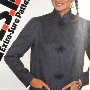 Puede incluir: Una mujer con una chaqueta gris oscuro con cuello mandarín y cierres de rana negros. La chaqueta tiene dos bolsillos delanteros y es parte de un Extra-Sure Pattern. La imagen incluye el número de patrón 5341.