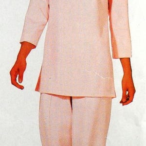 May include: A light pink two-piece set consisting of a long-sleeved tunic top with a boat neckline and matching straight-leg trousers. The outfit features a clean, solid-colored design with side slits on the tunic and a simple, structured silhouette.