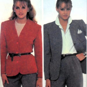 May include: Two women wearing blazers. The woman on the left is wearing a red blazer with a black belt and grey trousers. The woman on the right is wearing a grey blazer with a white collared shirt and grey trousers.