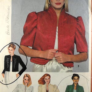 Puede incluir: Un sobre de patrón de costura con ilustraciones de varias chaquetas cortas con cuello alzado y mangas abullonadas. Los diseños incluyen una chaqueta roja de manga corta, una chaqueta negra bordada, una chaqueta blanca acolchada y una verde.