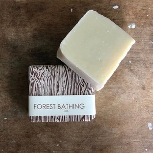 May include: A bar of soap wrapped in brown paper with a white woodgrain pattern. The label reads "FOREST BATHING 4 OZ."