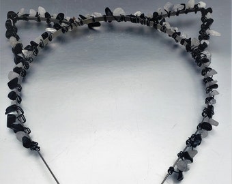 May include: A black and white headband with small stones and a wire frame. The headband is shaped like cat ears.