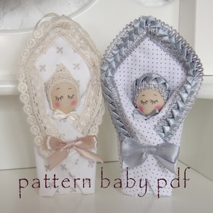 May include: Two handmade fabric baby dolls, one in a white and cream lace swaddle with a pink bow, and the other in a white and silver polka dot swaddle with a silver bow. The dolls have closed eyes and are lying down. The text "pattern baby pdf" is printed below the dolls.