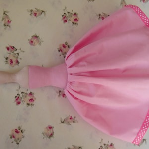 May include: A pink fabric doll with a white polka dot trim around the skirt. The doll has a wooden body and a pink fabric skirt.