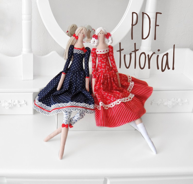 May include: Two handmade fabric dolls with blonde hair and red bows. The doll on the left is wearing a navy blue dress with white polka dots and white lace trim. The doll on the right is wearing a red dress with white polka dots and white lace trim. The dolls are sitting on a white surface. PDF tutorial.
