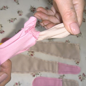 May include: A person is holding a pink fabric tube with a pencil. The fabric is folded and gathered at the top, creating a ruffle effect. The fabric is being used to create a garment or craft project.
