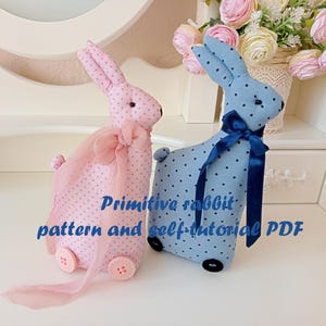 May include: Two handmade primitive rabbit toys, one pink with white polka dots and a pink ribbon, and one blue with white polka dots and a blue ribbon. The text "Primitive rabbit pattern and self-tutorial PDF" is printed below the toys.