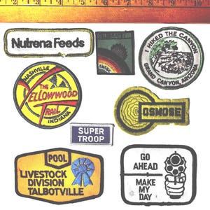 May include: A collection of embroidered patches with various designs and text. Patches include "Nutrena Feeds", "Celebrate", "I Hiked the Canyon Grand Canyon Arizona", "The Yellowwood Trail Indiana", "Osmose", "Super Troop", "Pool Livestock Division Talbotville", and "Go Ahead Make My Day".