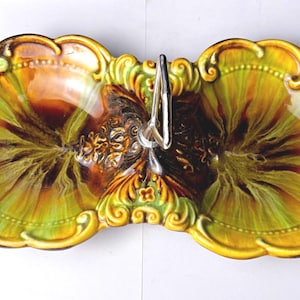 May include: A vintage two-section serving dish with a decorative handle. The dish features a vibrant color palette of yellow, green, and brown, with ornate, scrolled edges. The handle is silver-toned.