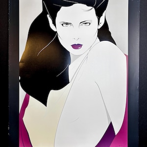 May include: A vintage art print featuring a stylized illustration of a woman with black hair and purple lipstick. The artwork has a minimalist style with bold lines and a limited color palette. The text "NAGEL THE BOOK" is at the bottom.