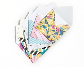 May include: A collection of open, decorative envelopes fanned out on a white surface. The envelopes feature various patterns, including stripes, floral designs, and gold accents. The color palette includes pink, yellow, teal, and white.