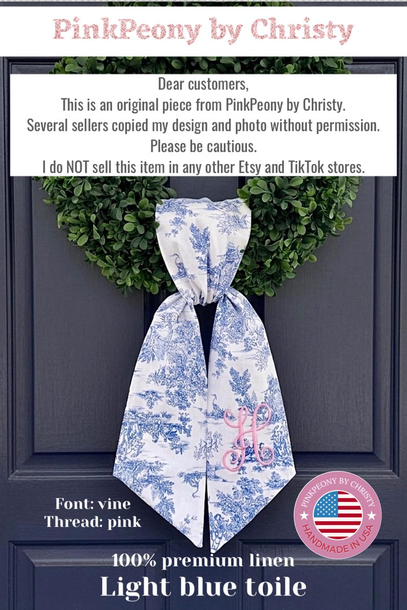 K&ouml;nnte beinhalten: Ein hellblaues Toile-de-Jouy-T&uuml;rschal aus Leinen mit einem rosa Monogramm, das an einer dunkelblauen T&uuml;r h&auml;ngt. Der Schal hat ein blau-wei&szlig;es Pastoraldesign. Der Text "PinkPeony by Christy" steht oben.