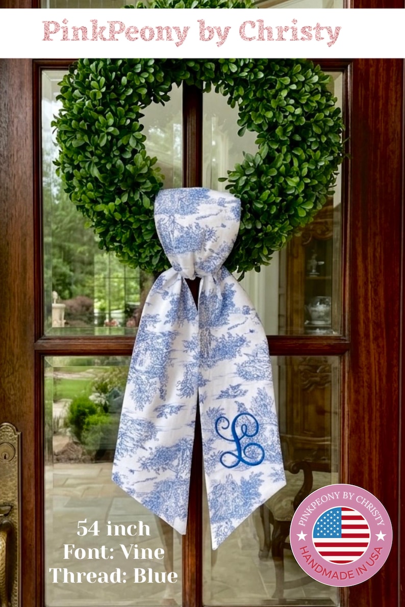 K&ouml;nnte beinhalten: Ein wei&szlig;-blau gemusterter Schal, ca. 137 cm lang, mit einem blau gestickten Initial. Der Schal wird an einer Glast&uuml;r mit einem gr&uuml;nen Kranz pr&auml;sentiert. Der Text "PinkPeony by Christy" steht oben.