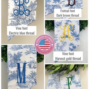 K&ouml;nnte beinhalten: Bestickte Stoffbanner mit blau-wei&szlig;em Toile-de-Jouy-Muster. Jedes Banner zeigt einen anderen Buchstaben in verschiedenen Schriftarten und Garnfarben, darunter elektrisches Blau, Dunkelbraun, Erntegold, Blau und Smaragdgr&uuml;n. Der Text auf den Bannern lautet "Vine font", "Fishtail font" und "Classic font".