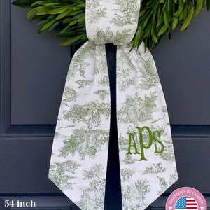 K&ouml;nnte beinhalten: Ein wei&szlig;-gr&uuml;ner T&uuml;rh&auml;nger im franz&ouml;sischen Toile-de-Jouy-Stil mit pastoralem Szenenmuster. Die Initialen "APS" sind in Moosgr&uuml;n gestickt. Hergestellt aus 100 % Premium-Leinen.