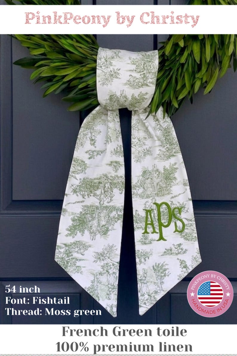 K&ouml;nnte beinhalten: Ein wei&szlig;-gr&uuml;ner T&uuml;rh&auml;nger im franz&ouml;sischen Toile-de-Jouy-Stil mit pastoralem Szenenmuster. Die Initialen "APS" sind in Moosgr&uuml;n gestickt. Hergestellt aus 100 % Premium-Leinen.