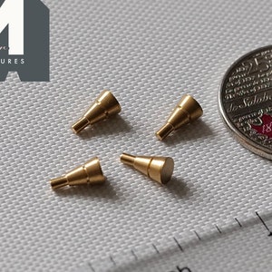 May include: Four small gold-colored metal cones, each about 1/2 inch in length, are arranged on a white surface. A ruler and a Canadian coin are also visible in the image.