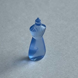 May include: A small, light blue, translucent dress form figurine. The miniature dress form has a rounded base and a detailed bodice, with a small, rounded head. The figurine is made of a clear, possibly acrylic material.