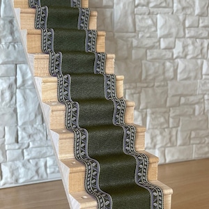 May include: A wooden staircase with a dark green carpet runner featuring a leaf pattern. The staircase is against a white brick wall.