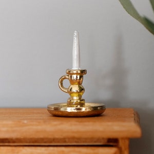 Könnte beinhalten: Ein goldener Kerzenständer mit einer weißen Kerze auf einer Holzoberfläche.