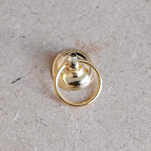 May include: Gold door knob with a round ring handle. The knob is a decorative piece for dollhouses or miniature projects.