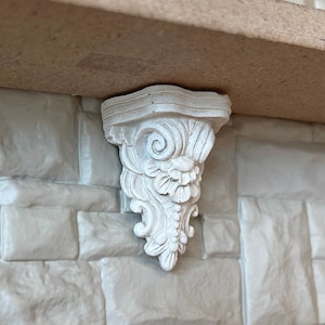 May include: White decorative shelf bracket with intricate floral and scrollwork details. The bracket is made of a lightweight material and is designed to support a shelf.